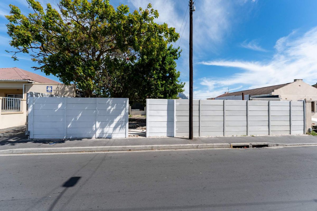 Street view of the property frontage featuring a precast concrete boundary wall with a central opening and adjacent asphalt road.