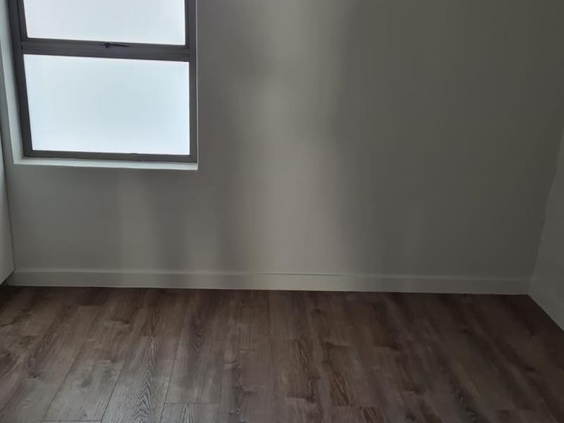 A bright, empty bedroom featuring modern wood-look laminate flooring and a frosted glass window, providing a clean and neutral canvas.