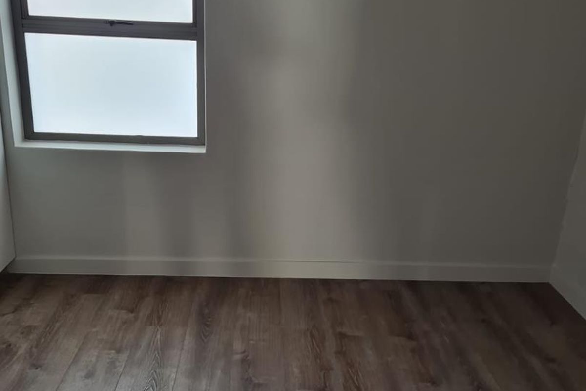 A bright, empty bedroom featuring modern wood-look laminate flooring and a frosted glass window, providing a clean and neutral canvas.