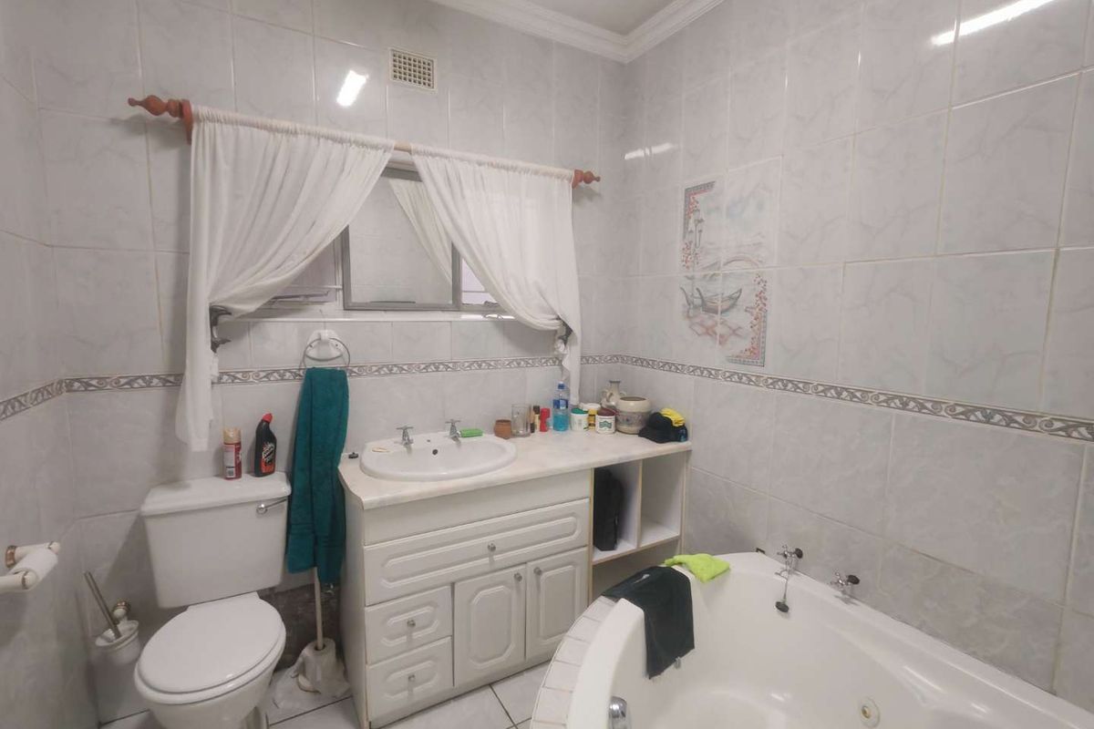A functional bathroom featuring a built-in vanity with basin, a corner bathtub, and full-height wall tiling.