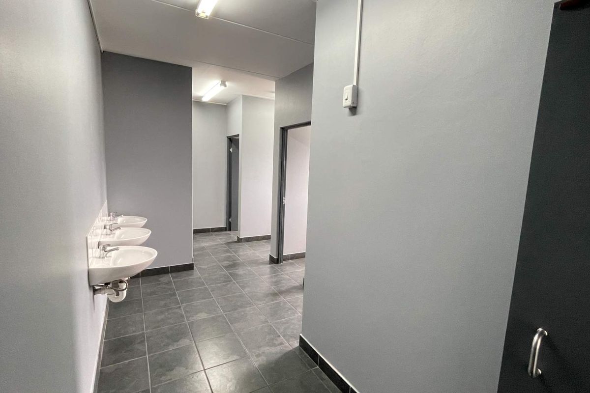 A clean, modern industrial washroom facility featuring multiple wall-mounted ceramic basins, tiled flooring, and neutral grey wall finishes.