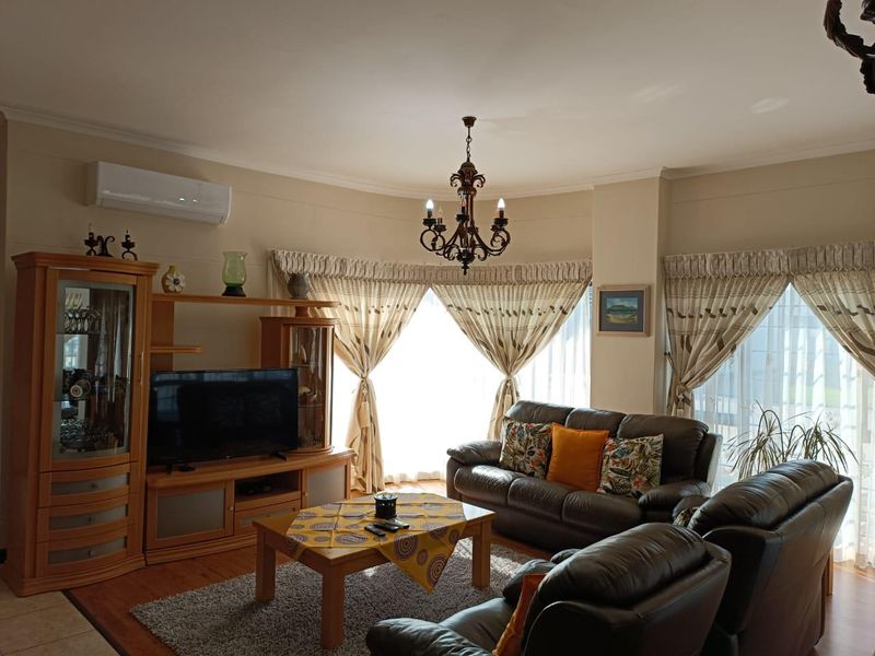 A comfortable living room featuring laminate flooring, a central chandelier, and a wall-mounted split-system air conditioner with large windows allowing natural light.