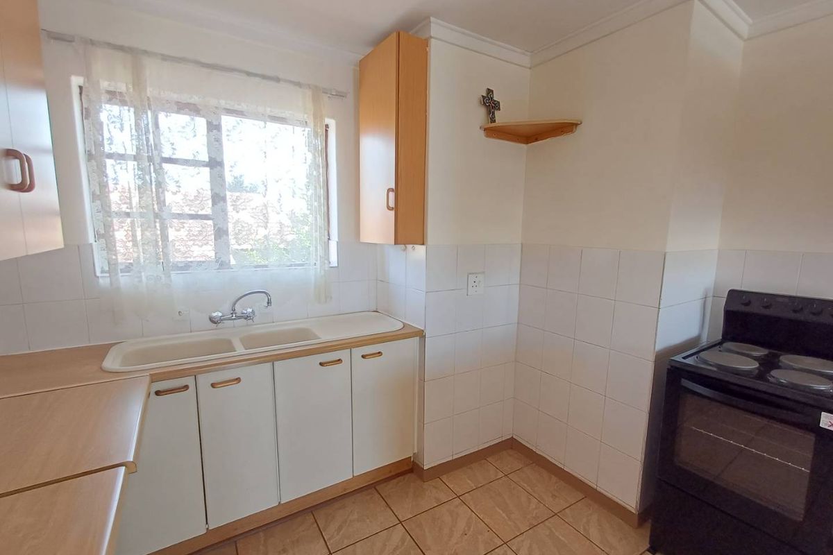 A functional kitchen featuring light wood-tone cabinetry, a double basin sink, tiled splashbacks, and space for a freestanding stove.