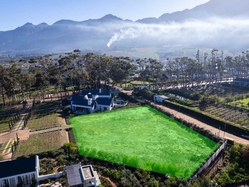 An aerial view of a vacant residential plot highlighted in green, situated in a scenic estate with mountain views.