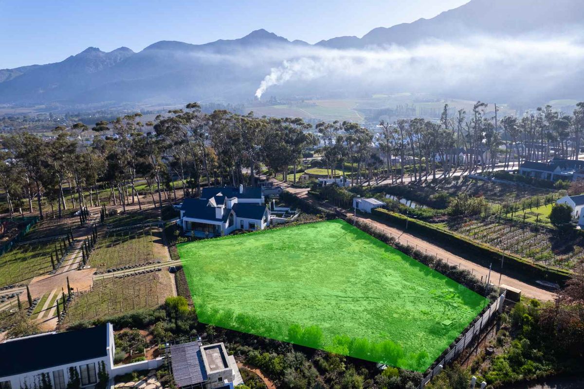 An aerial view of a vacant residential plot highlighted in green, situated in a scenic estate with mountain views.