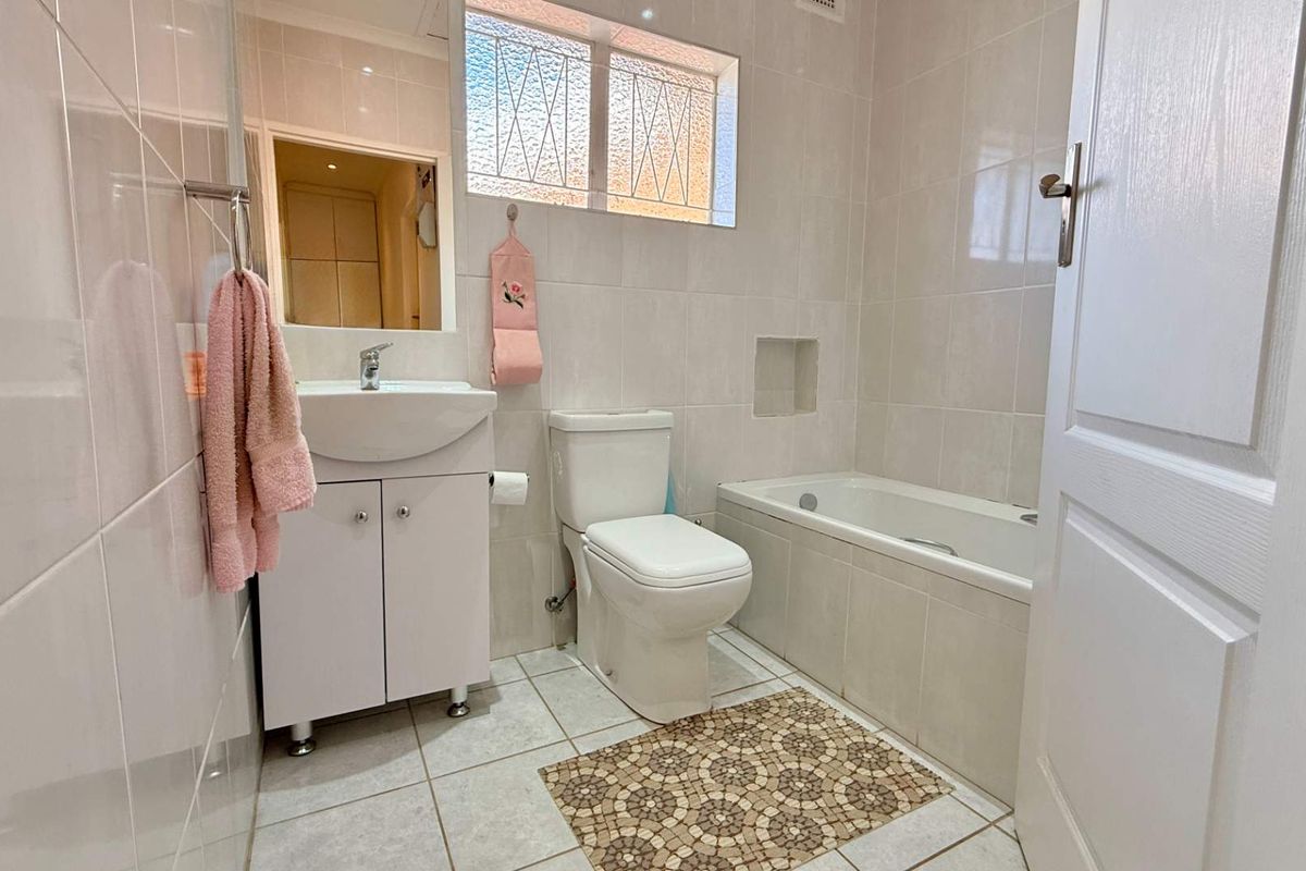 A clean, functional bathroom featuring a built-in bathtub, vanity cabinet with basin, toilet, and neutral wall and floor tiling.