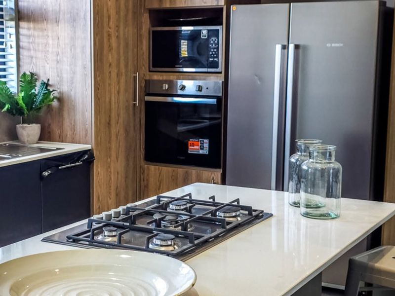 Modern kitchen featuring wood-grain cabinetry, a central island with a gas hob, stone countertops, and integrated built-in appliances.
