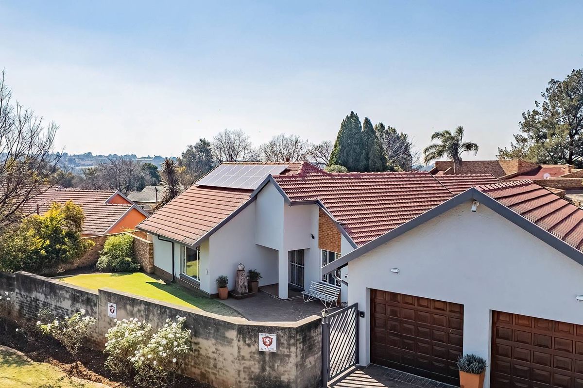 Aerial view of a residential property featuring a tiled roof with solar panels, a double garage, and a secure perimeter wall.