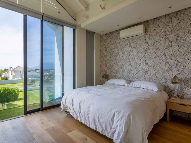 A bright bedroom featuring hardwood flooring, a vaulted ceiling, and large sliding glass doors that open to an outdoor balcony with scenic views.