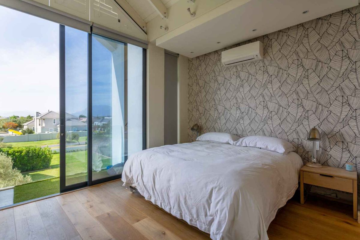 A bright bedroom featuring hardwood flooring, a vaulted ceiling, and large sliding glass doors that open to an outdoor balcony with scenic views.