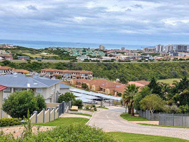 Elevated view overlooking a residential estate with paved access roads, carport structures, and distant coastal scenery.
