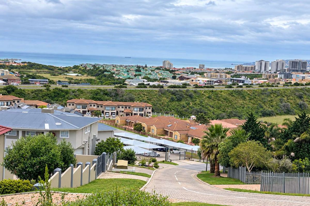 Elevated view overlooking a residential estate with paved access roads, carport structures, and distant coastal scenery.