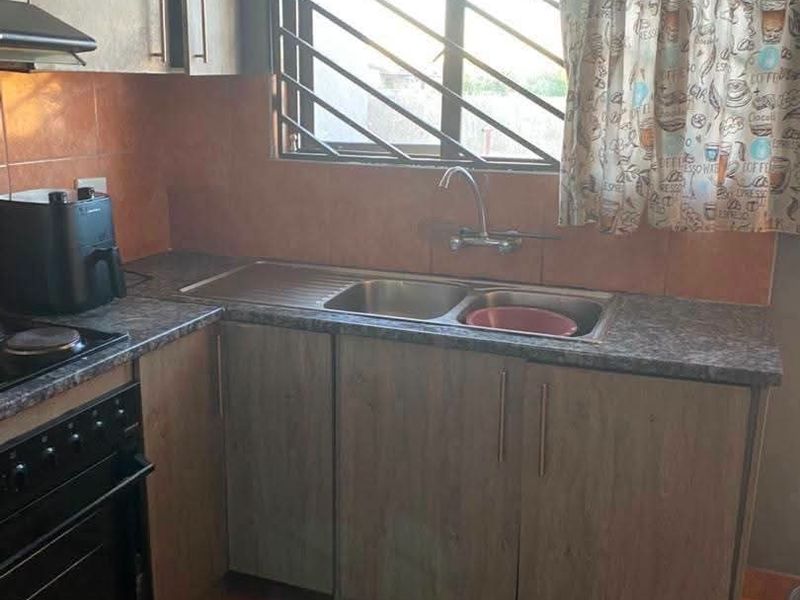 A functional kitchen featuring laminate cabinetry, a stainless steel sink, built-in oven with hob, extractor fan, and tiled flooring.