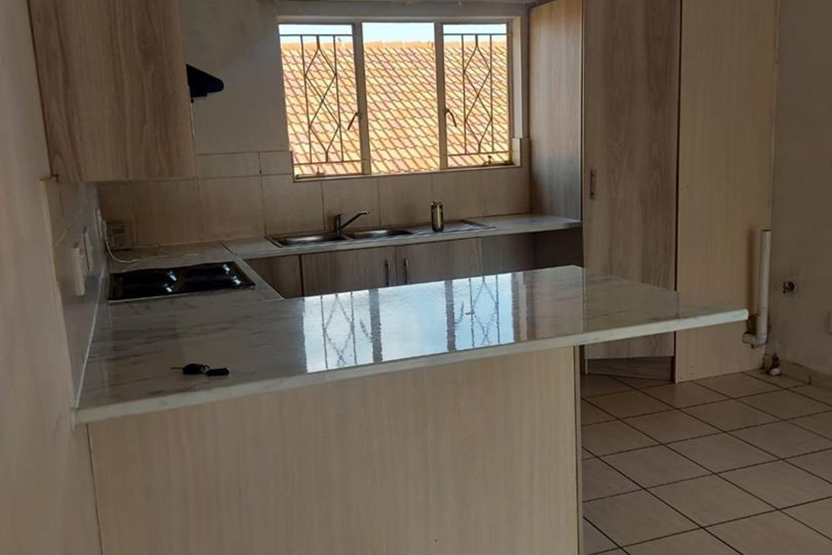 A functional kitchen featuring light wood-look cabinetry, marble-effect countertops, a built-in hob, and tiled flooring with a window overlooking the exterior.