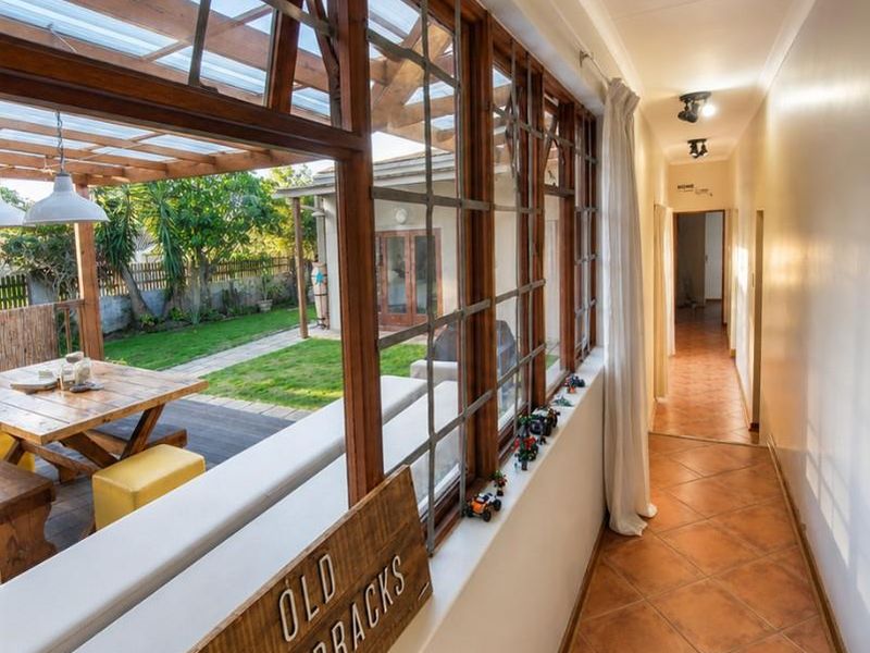 A bright hallway featuring terracotta floor tiles and large timber-framed windows that provide a view of the outdoor patio and garden area.