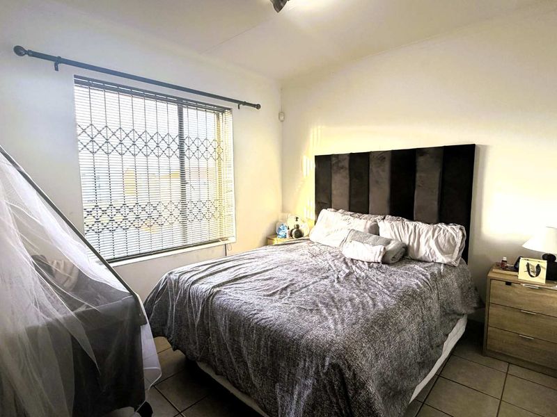 A functional bedroom featuring tiled flooring, a window with security gate and venetian blinds, providing a neutral space for rest.