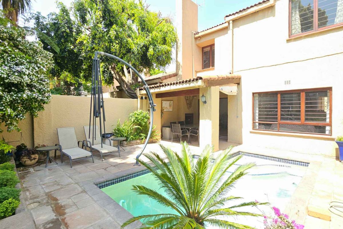 Rear exterior view featuring a swimming pool, covered patio area, and established garden space.