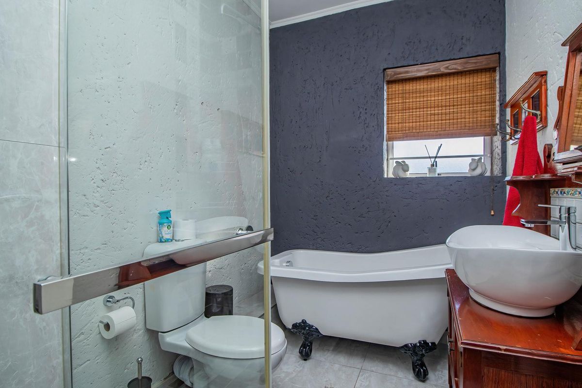 A bathroom featuring a freestanding clawfoot bathtub, a glass-enclosed shower, a toilet, and a vessel sink vanity with a dark accent wall.