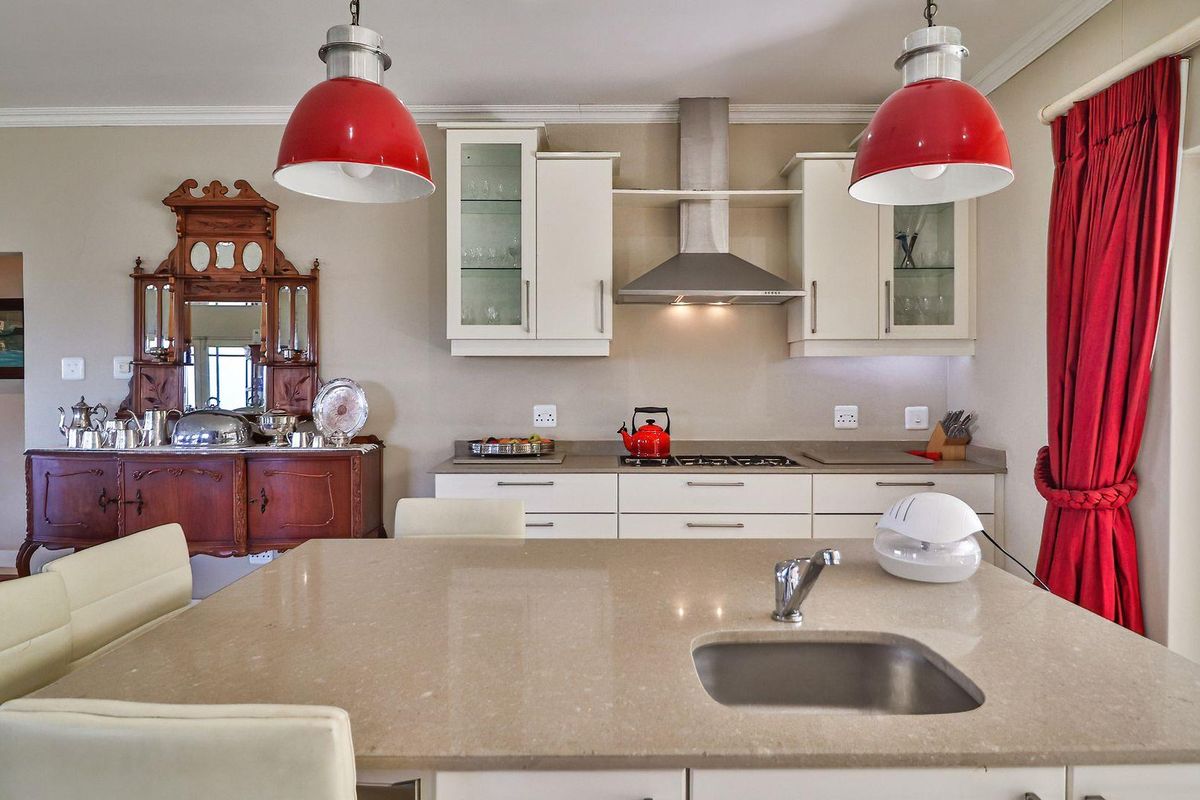 Modern kitchen featuring a central island with a stainless steel sink, stone countertops, built-in cabinetry, and a stainless steel extractor fan.