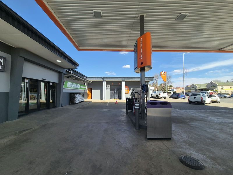 A well-maintained commercial fuel station forecourt featuring a modern canopy, fuel pumps, and access to adjacent retail and restroom facilities.