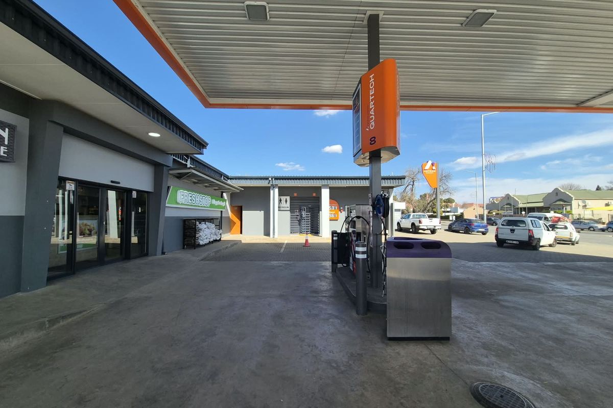 A well-maintained commercial fuel station forecourt featuring a modern canopy, fuel pumps, and access to adjacent retail and restroom facilities.