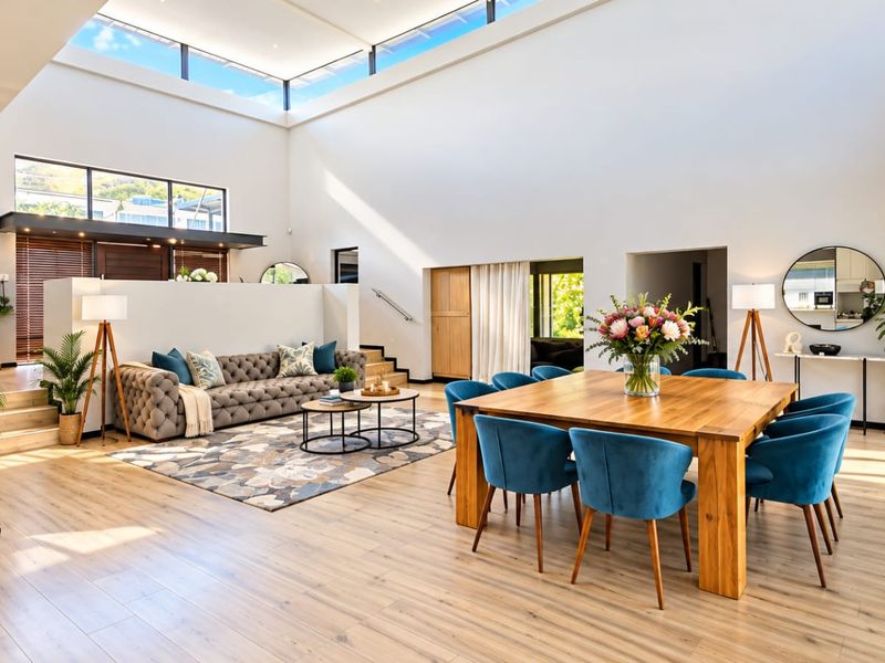 Spacious open-plan living and dining area featuring high ceilings, a large skylight, modern laminate flooring, and seamless access to outdoor spaces through sliding glass doors.