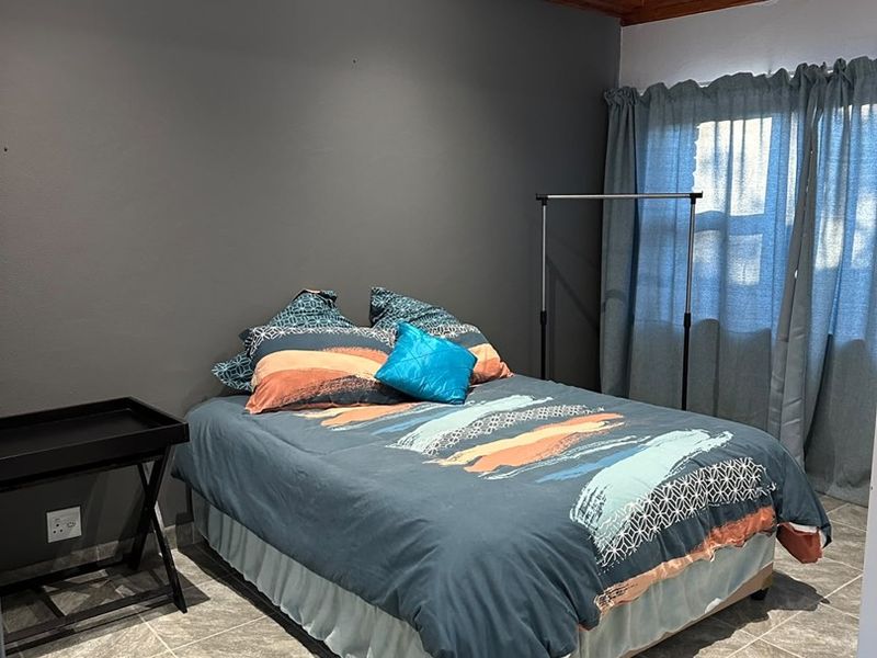 A bedroom featuring tiled flooring, exposed timber ceiling beams, and a dark accent wall, providing a neutral base for interior design.