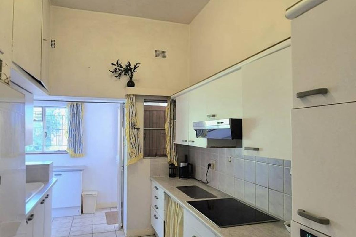 A functional galley-style kitchen featuring white built-in cabinetry, tiled flooring, an integrated oven, and an electric cooktop with an extractor fan.