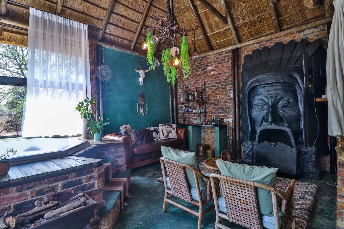 Unique living space featuring a thatched roof, exposed brick walls, a built-in fireplace with decorative surround, and an integrated corner bathtub.