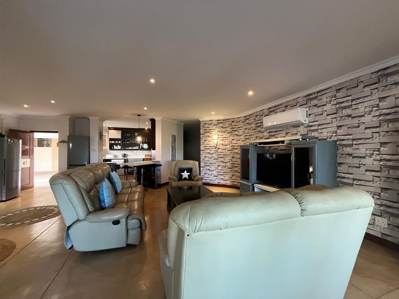 Spacious open-plan living area featuring a stone-cladding accent wall, recessed lighting, and a seamless transition to the kitchen space.