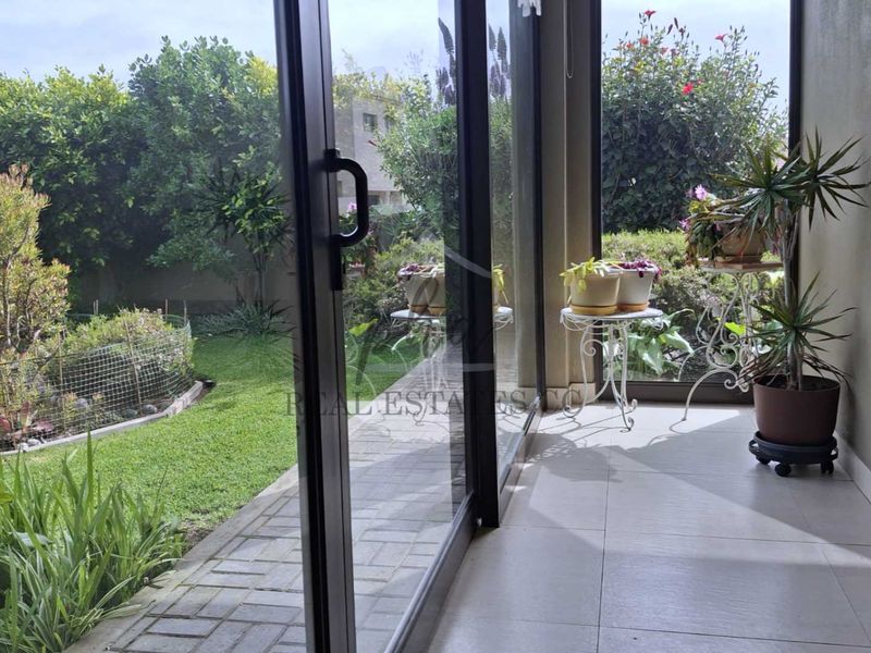 A covered patio area featuring tiled flooring and large sliding glass doors that open onto a landscaped garden and paved walkway.