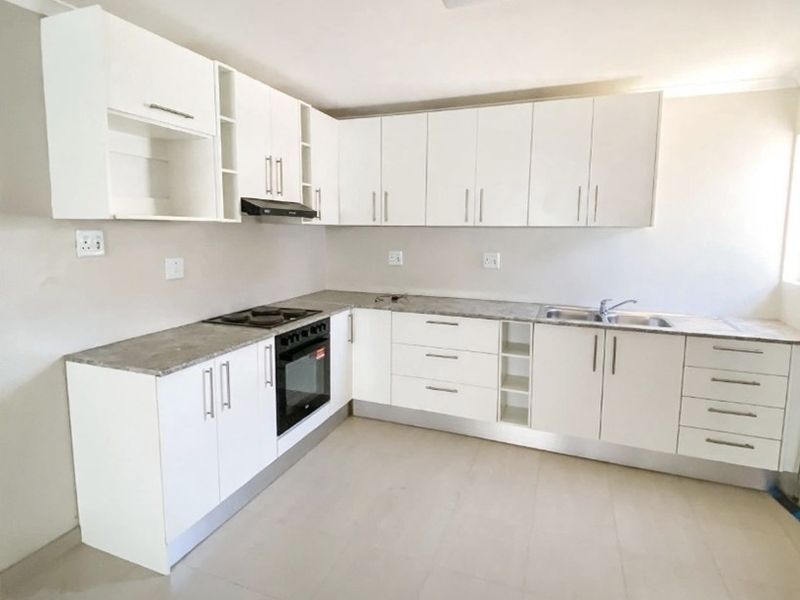 A clean, modern kitchen featuring white built-in cabinetry, stone-look countertops, integrated oven and hob, and neutral tiled flooring.