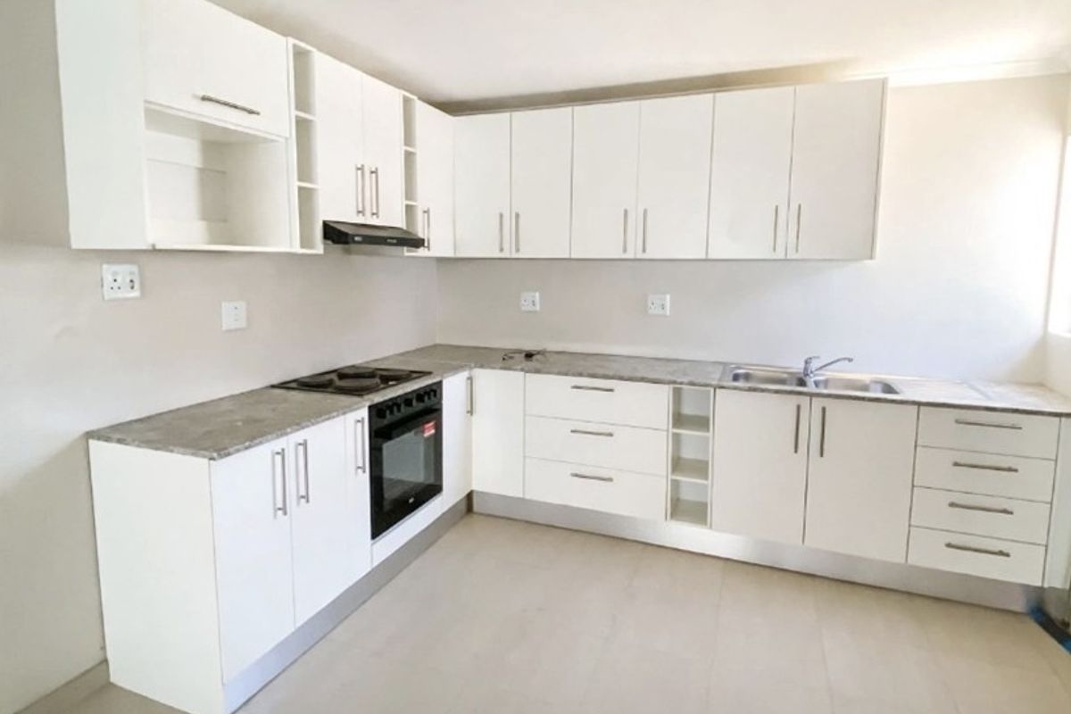 A clean, modern kitchen featuring white built-in cabinetry, stone-look countertops, integrated oven and hob, and neutral tiled flooring.