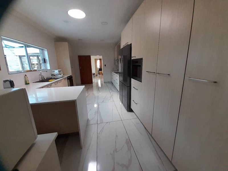 Modern kitchen featuring light wood cabinetry, stone countertops, integrated appliances, and polished marble-look porcelain floor tiles.