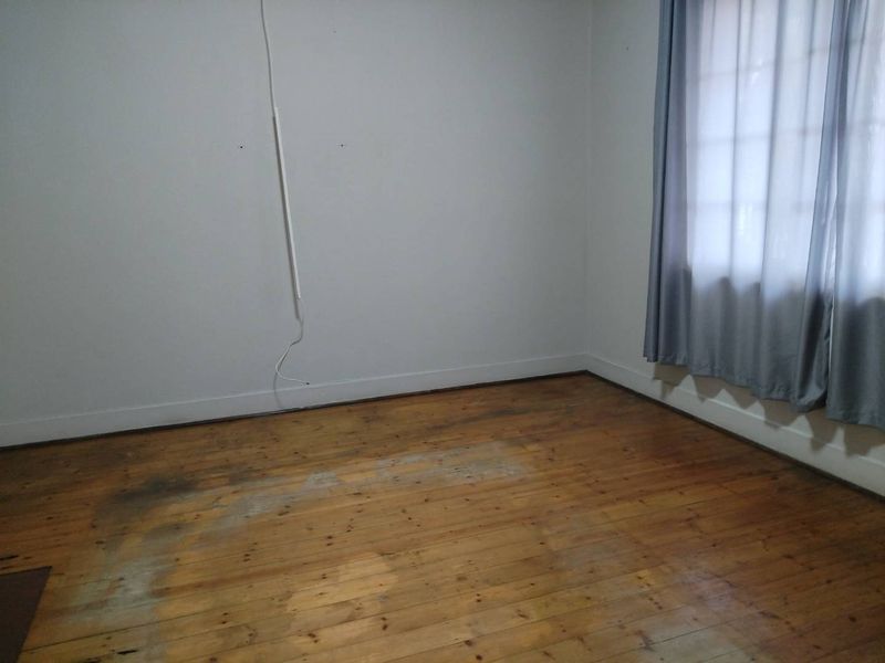 An empty bedroom featuring original timber flooring, neutral walls, and window treatments, requiring some cosmetic updates to restore its appeal.