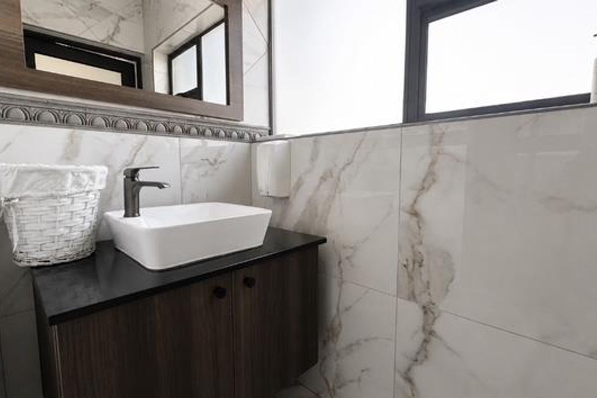 Modern bathroom featuring a sleek vessel sink, dark wood vanity cabinet, stone countertop, and elegant marble-look wall tiling.