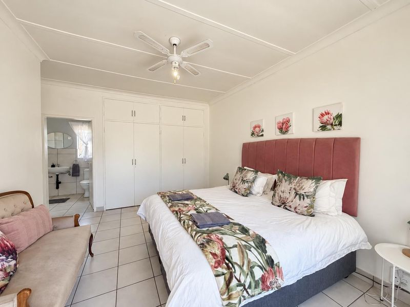 Spacious bedroom featuring built-in cupboards, tiled flooring, a ceiling fan, and direct access to an en-suite bathroom.