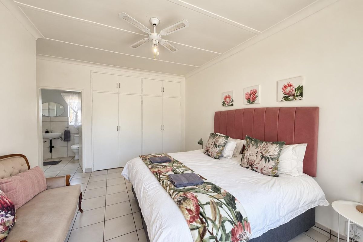Spacious bedroom featuring built-in cupboards, tiled flooring, a ceiling fan, and direct access to an en-suite bathroom.