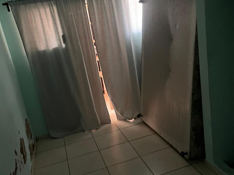 A bedroom featuring tiled flooring and a sloped ceiling, currently requiring wall repairs and repainting to restore the space.