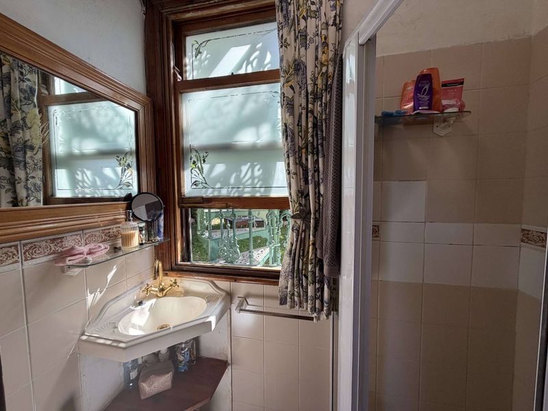 A compact bathroom featuring a corner basin, shower enclosure, and tiled walls, with a timber-framed window providing natural light.