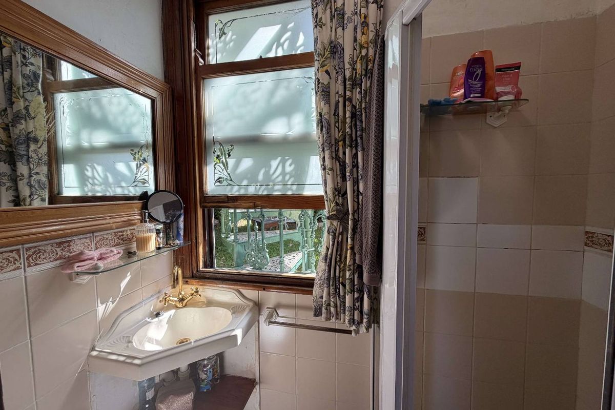 A compact bathroom featuring a corner basin, shower enclosure, and tiled walls, with a timber-framed window providing natural light.