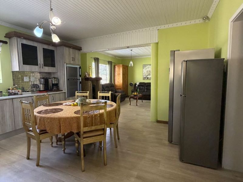 Open-plan kitchen and dining area featuring light wood-look flooring, tongue and groove ceiling, and functional built-in cabinetry with a tiled backsplash.