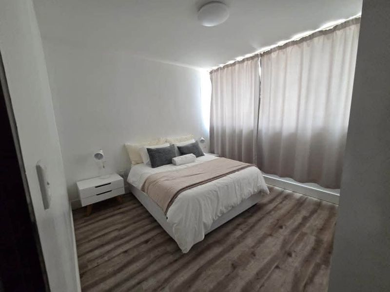 A well-maintained bedroom featuring modern laminate flooring, neutral wall finishes, and floor-to-ceiling curtains.