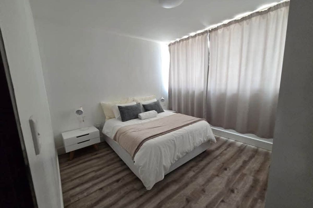 A well-maintained bedroom featuring modern laminate flooring, neutral wall finishes, and floor-to-ceiling curtains.