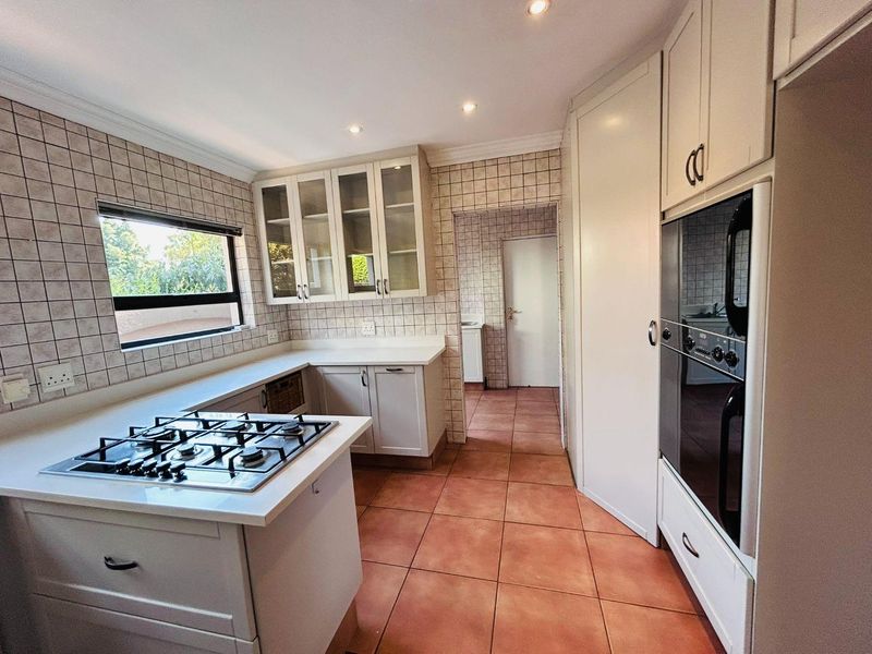A functional kitchen featuring a gas hob, built-in oven, stone countertops, and ample cabinetry, with a tiled splashback and terracotta-style floor tiles.