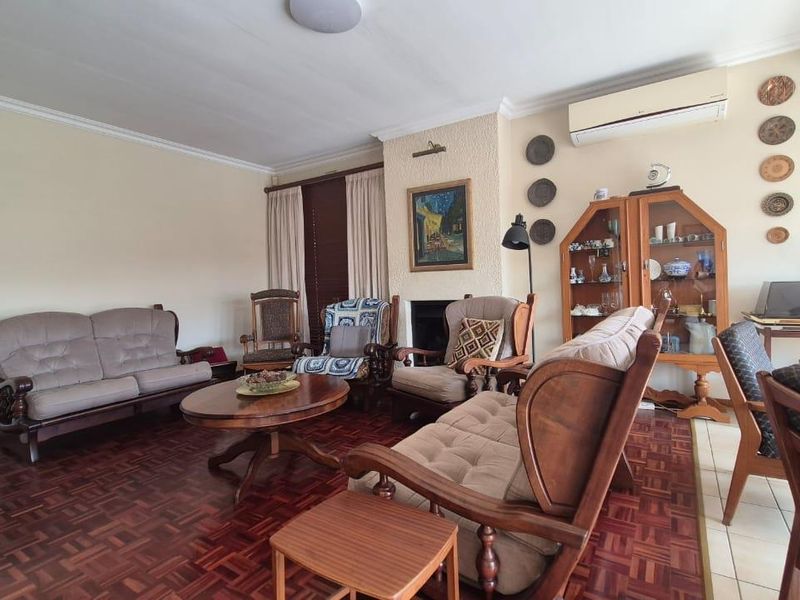 A spacious living room featuring traditional parquet flooring, a central fireplace, and a wall-mounted air conditioning unit.