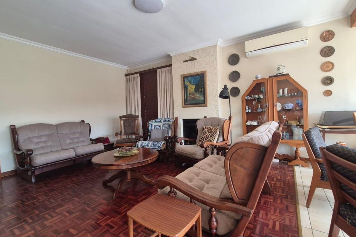 A spacious living room featuring traditional parquet flooring, a central fireplace, and a wall-mounted air conditioning unit.