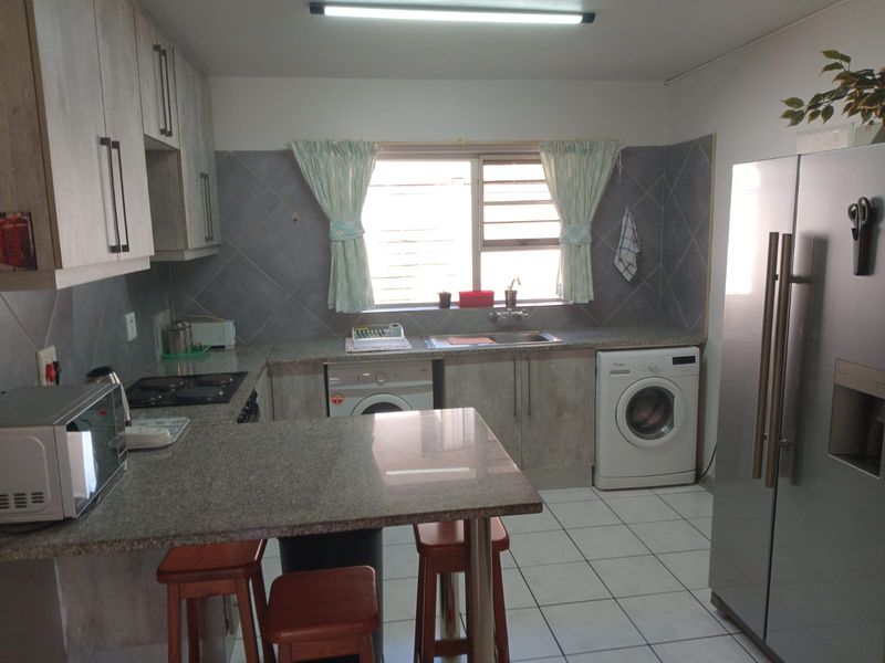 A functional kitchen featuring granite countertops, built-in cabinetry, tiled backsplash, and integrated laundry appliance connections.