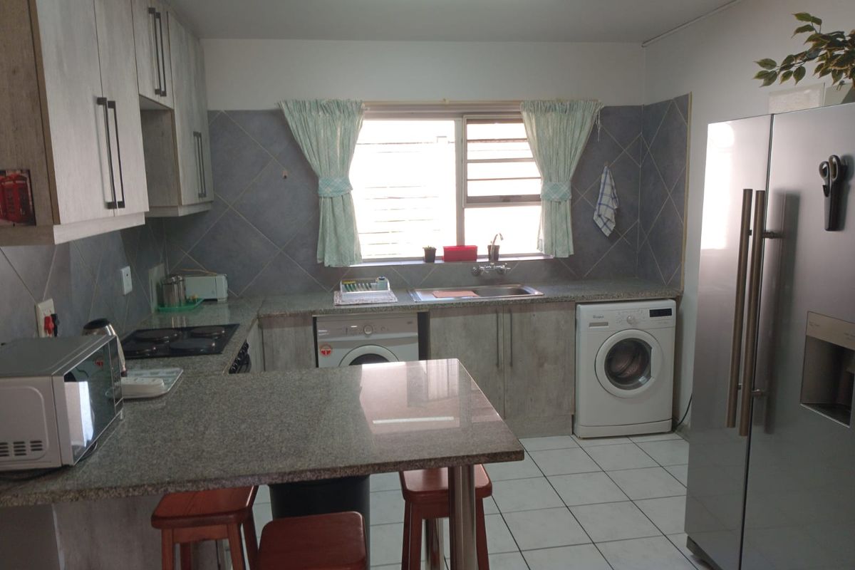 A functional kitchen featuring granite countertops, built-in cabinetry, tiled backsplash, and integrated laundry appliance connections.