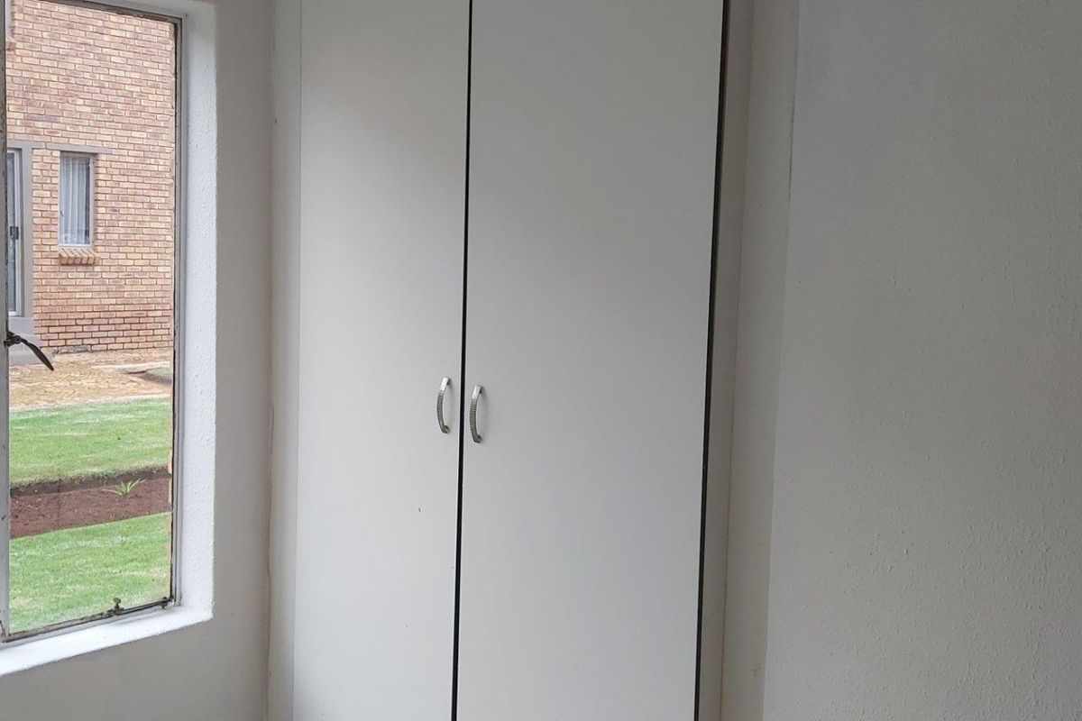 A bedroom featuring built-in white cabinetry and a large window overlooking the complex garden area.